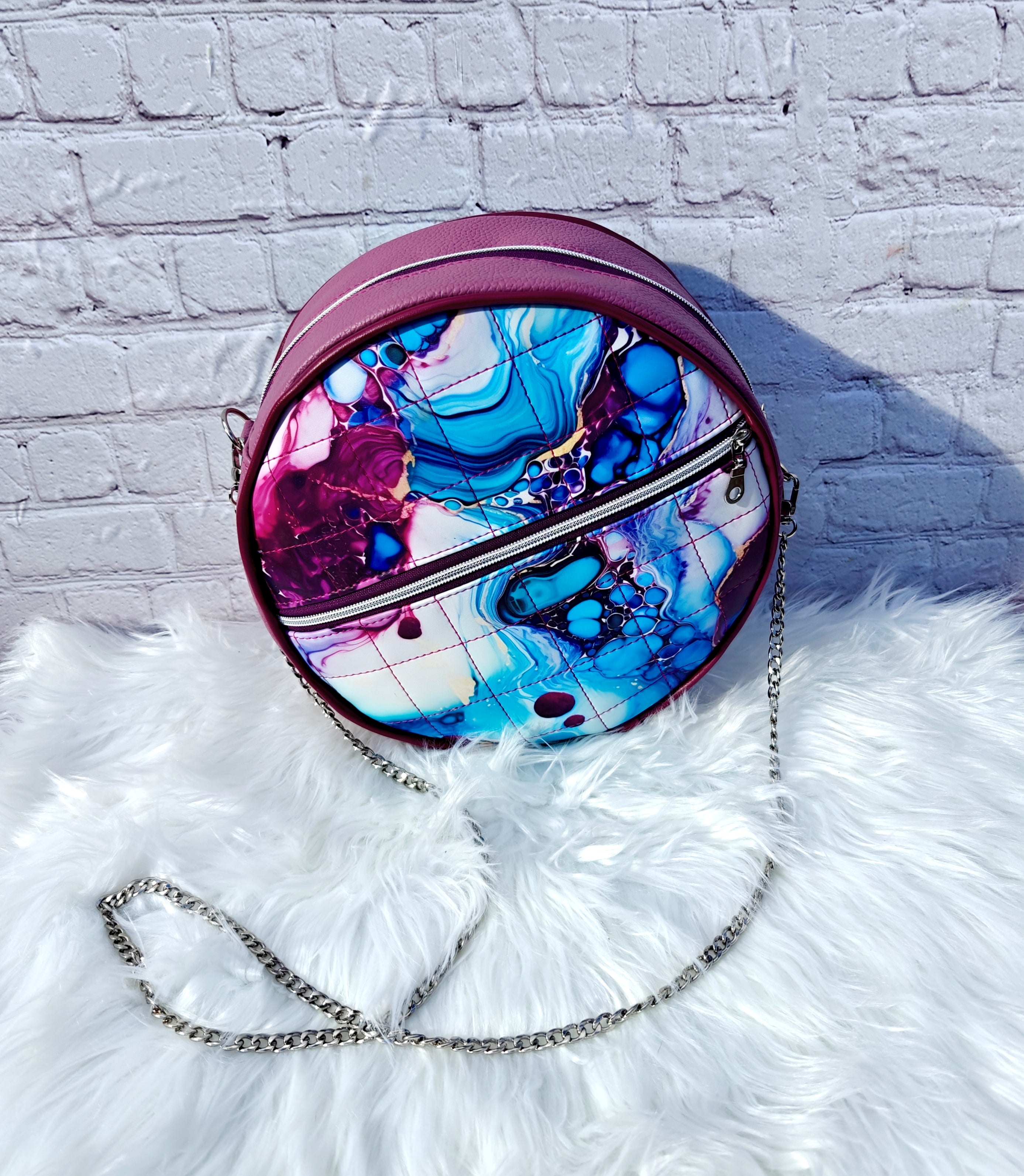 Handcrafted round vinyl bag in mauve purple with silver hardware and hidden strap connectors.