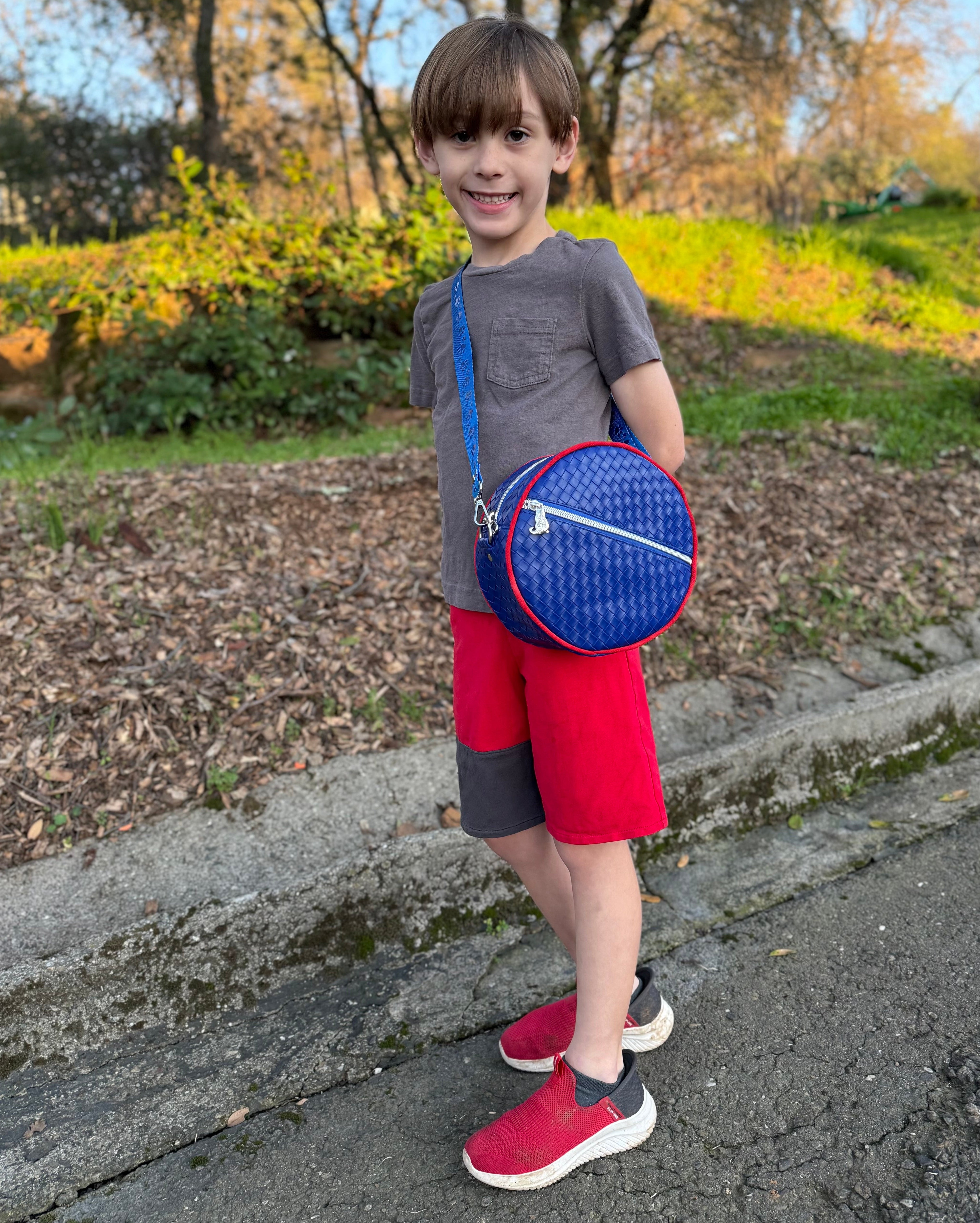 boy wearing the Small Ellie Round Bag in quilted vinyl blue fabric with a blue strap and red piping.