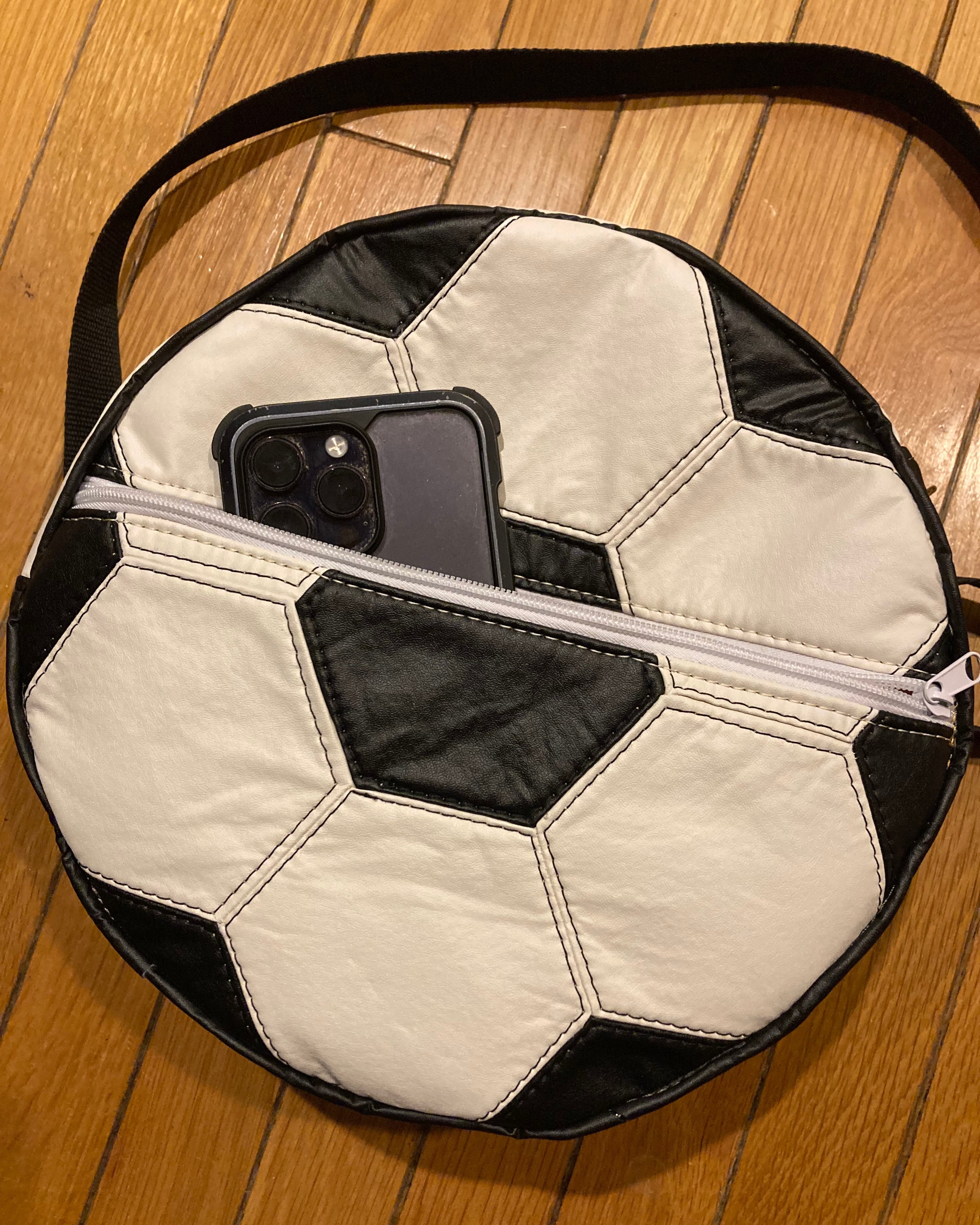 Soccer ball-shaped bag with a phone inside on a wooden floor