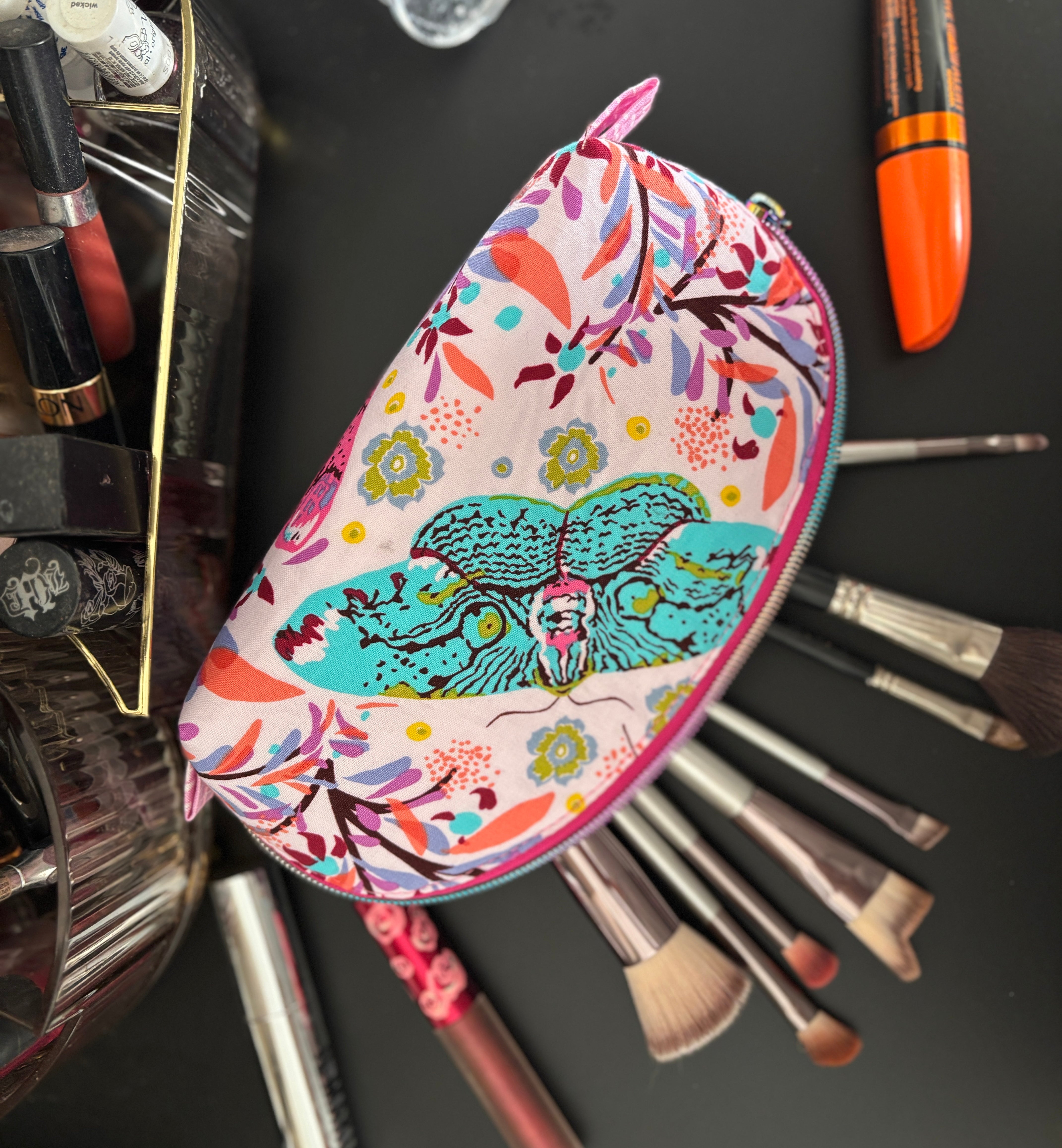 Colorful makeup case with floral and animal design surrounded by makeup brushes and tools on a dark background. Easy sewing pattern for travel bags.
