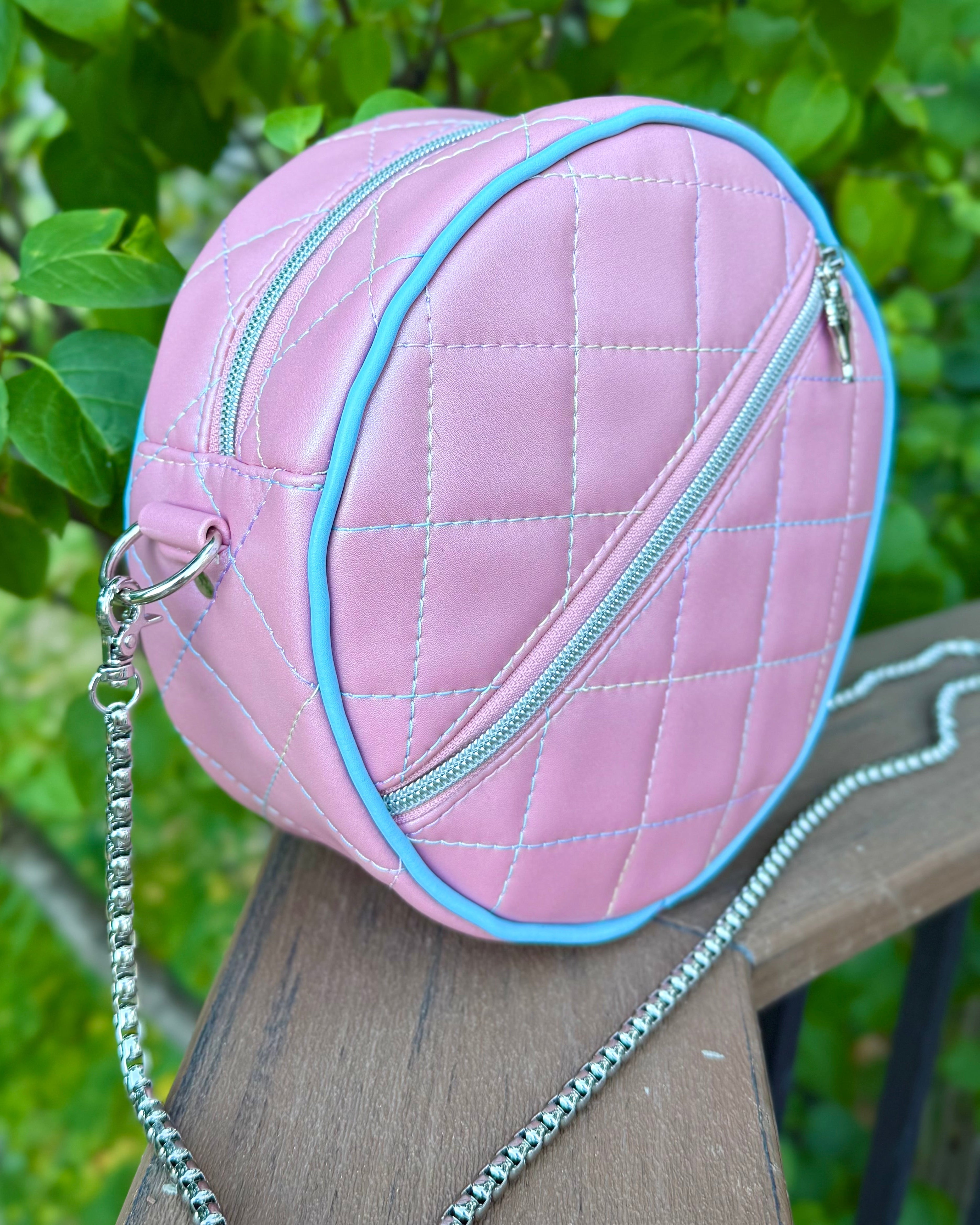 Pink quilted vinyl handbag with a chain strap on a wooden surface with green leaves in the background