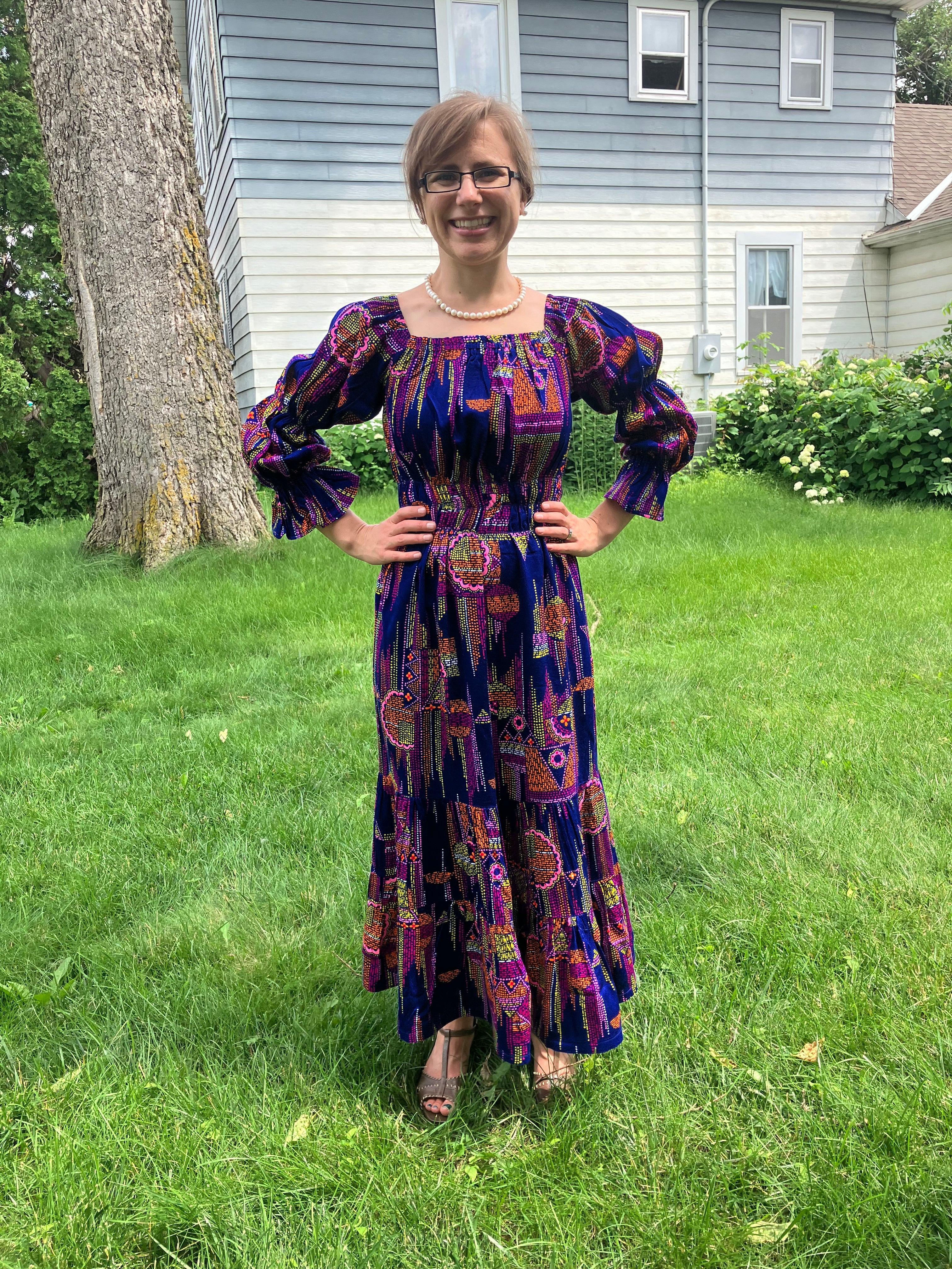 Person wearing a colorful long sleeve woven midi dress standing on grass with a house in the background.