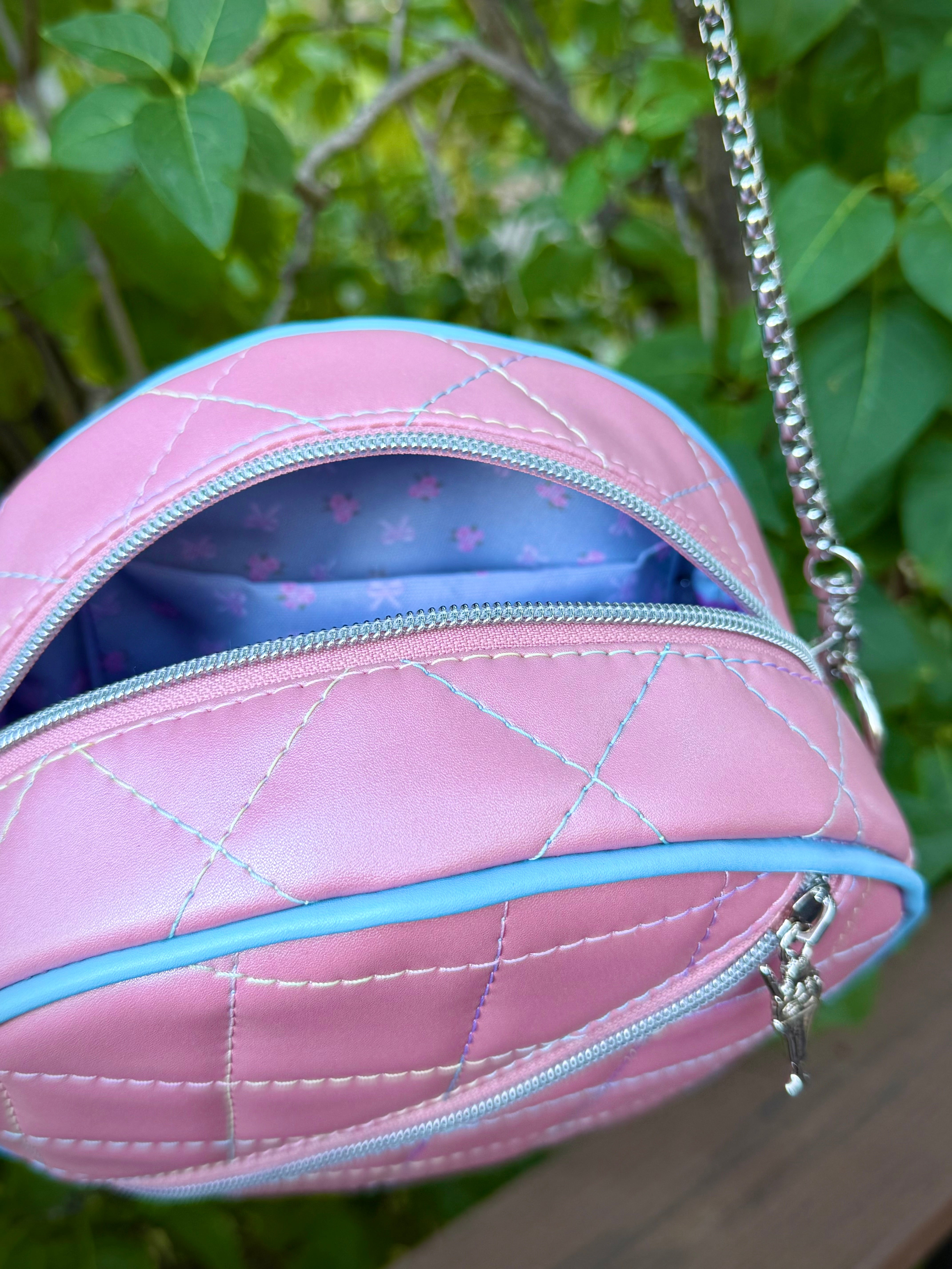 Pink quilted handbag with a chain strap, showing inside view, against a green leafy background.