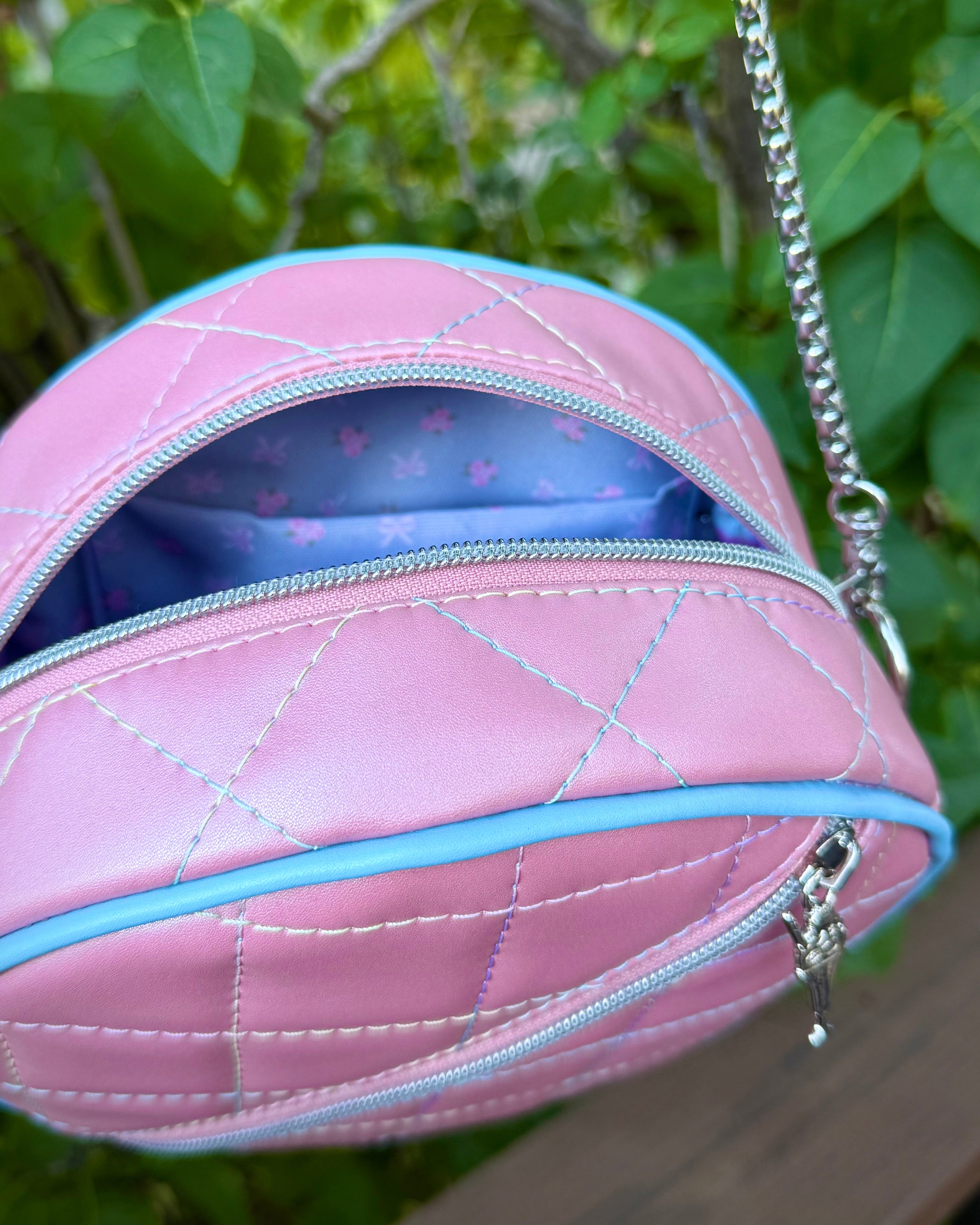 Pink quilted handbag with a chain strap, showing inside view, against a green leafy background.