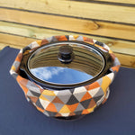 Decorative crock pot carrier bag with geometric pattern on a blue and wooden background. This carrier was made using the warm and cozy slow cooker carrier pattern by Ellie and Mac sewing patterns.