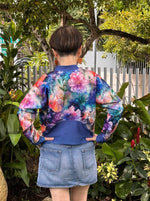 Woman outside modeling a floral and blue athletic bomber jacket with zip closure, kangaroo pocket detail, and cuffs. Easy pdf sewing pattern.