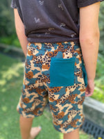 Person wearing camouflage shorts with a blue pocket in an outdoor setting made using the Caleb Athletic Sewing Pattern by Ellie and Mac Patterns.