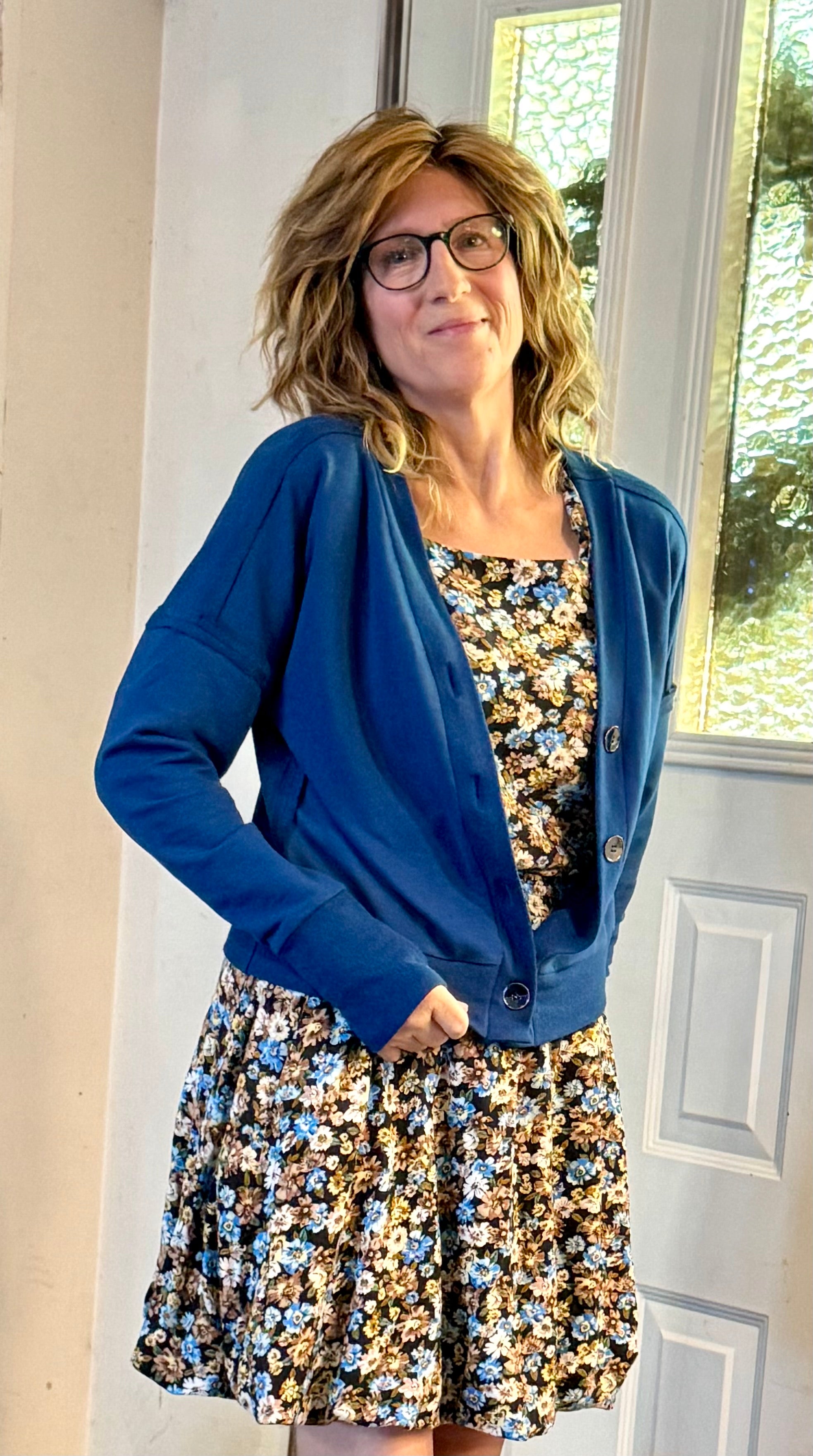 Woman wearing a blue cardigan over a floral dress indoors.