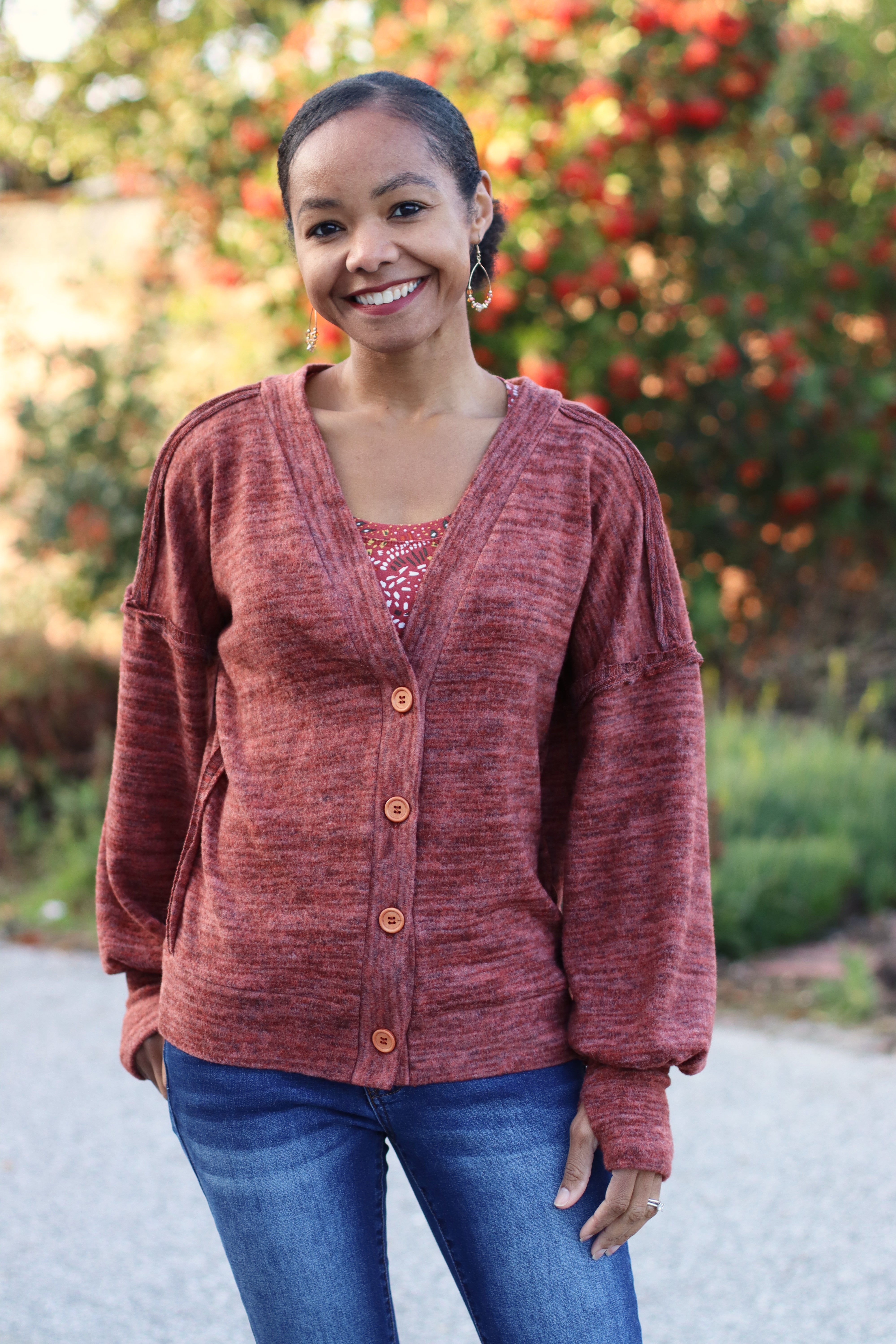 Woman wearing a maroon cardigan  with bishop sleeves and thumbhole cuffs with a blurred outdoor background.
