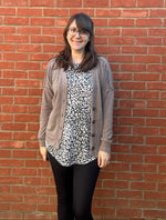 Person standing on a red brick pavement wearing glasses and a patterned shirt with a boxy cardigan over. 