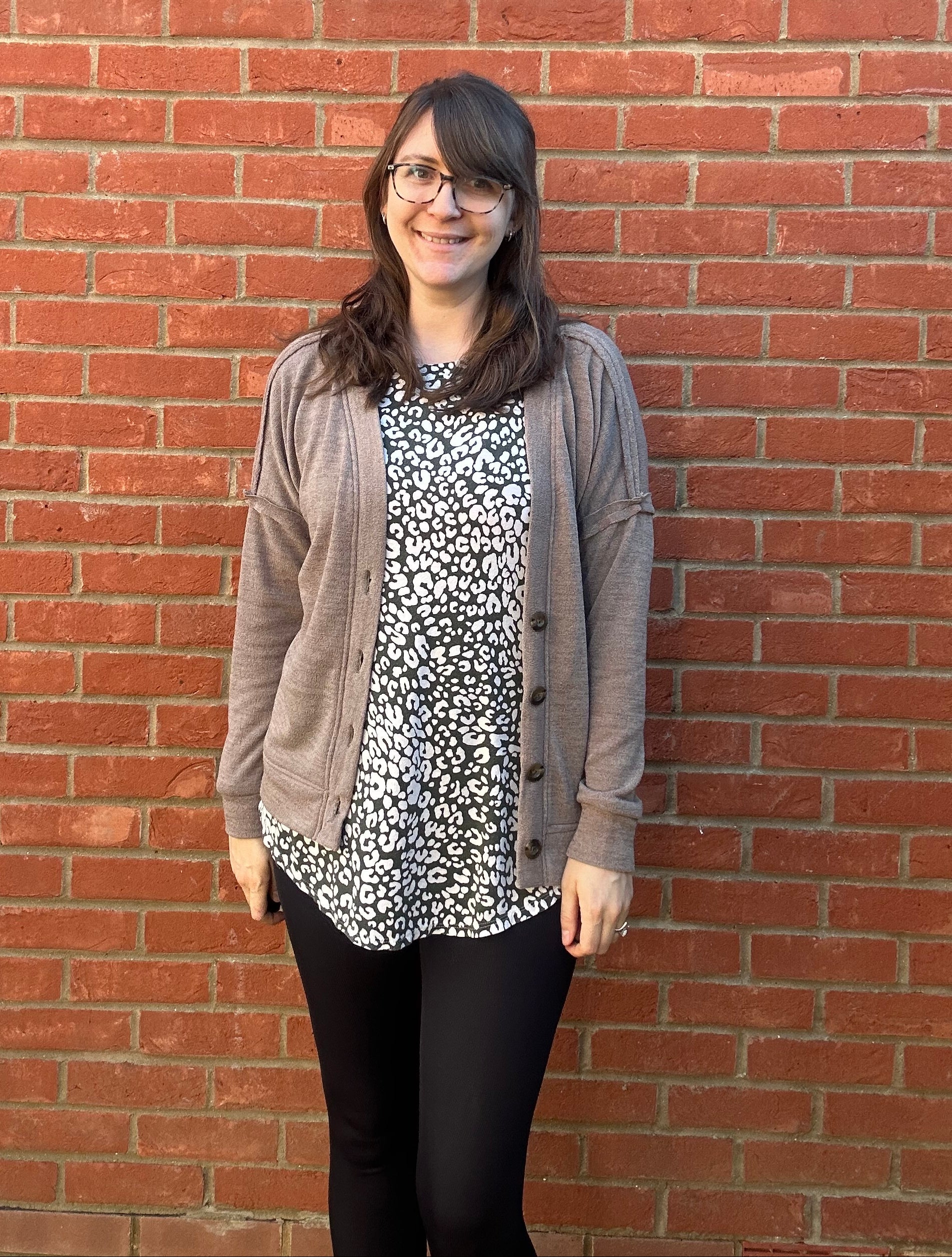 Person standing on a red brick pavement wearing glasses and a patterned shirt with a boxy cardigan over. 