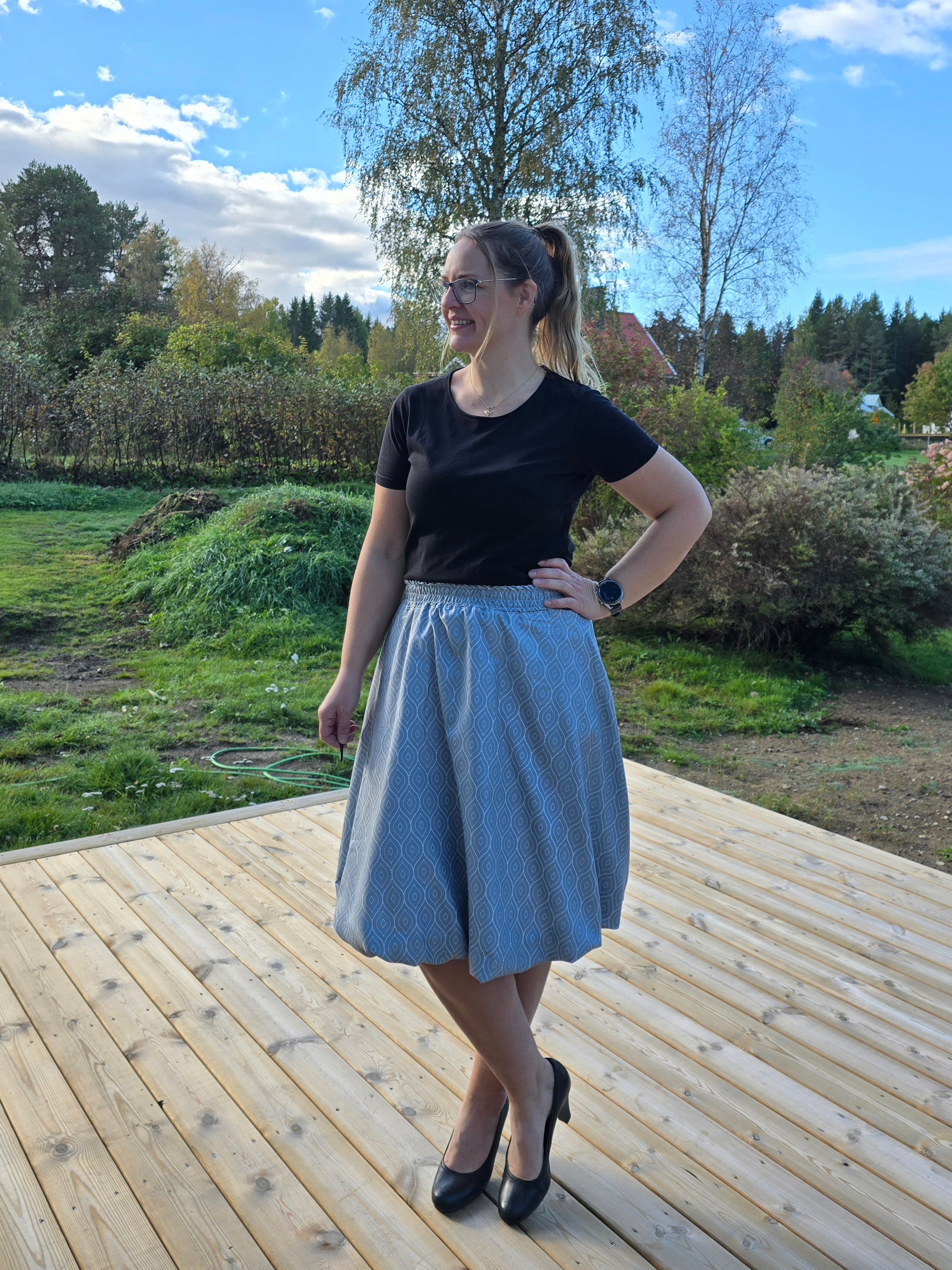 Woman standing on a wooden deck with trees and grass in the background. Fast sewing project for woven fabrics.