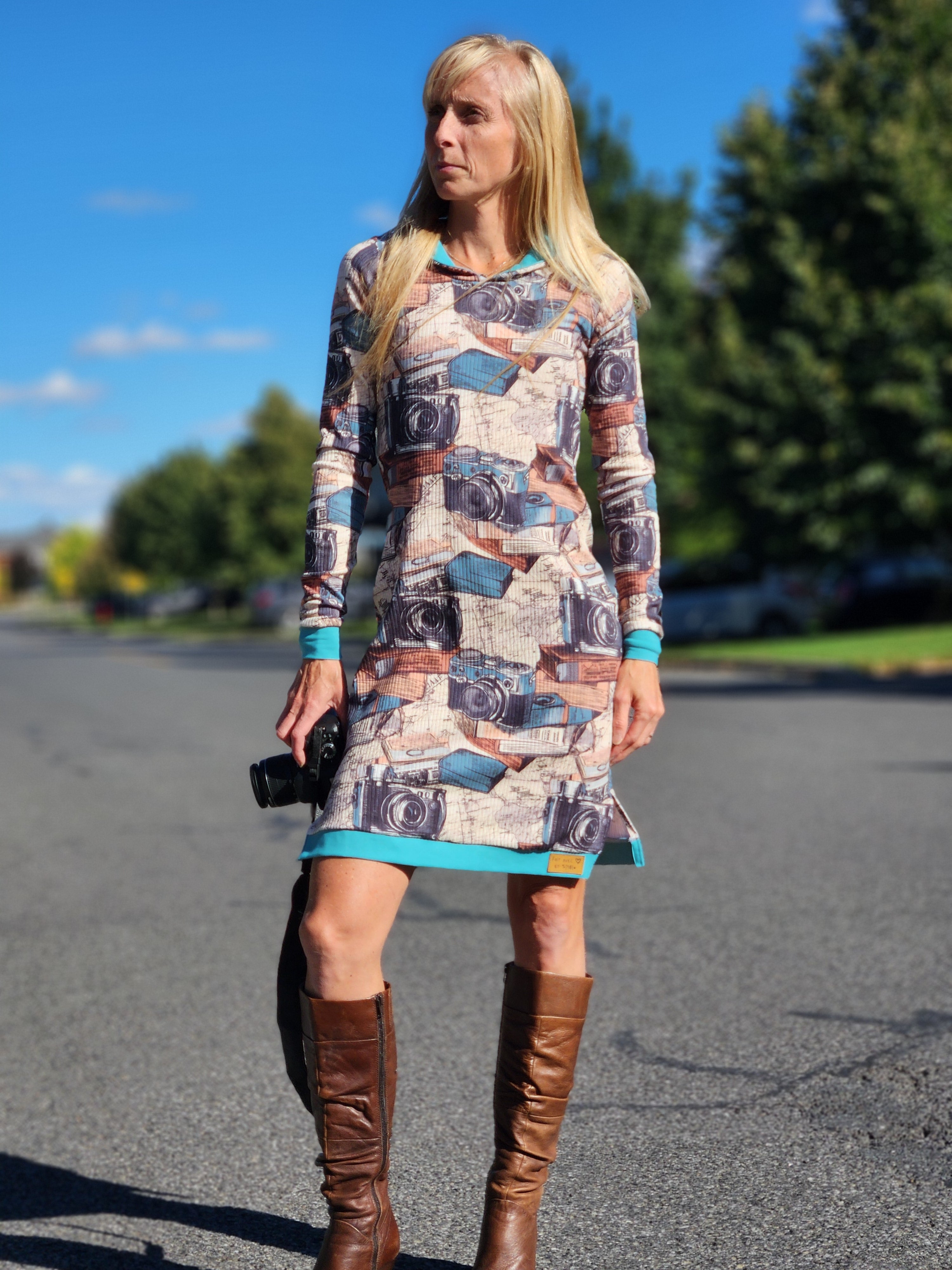 Woman in a patterned dress and brown boots standing on a road with trees in the background