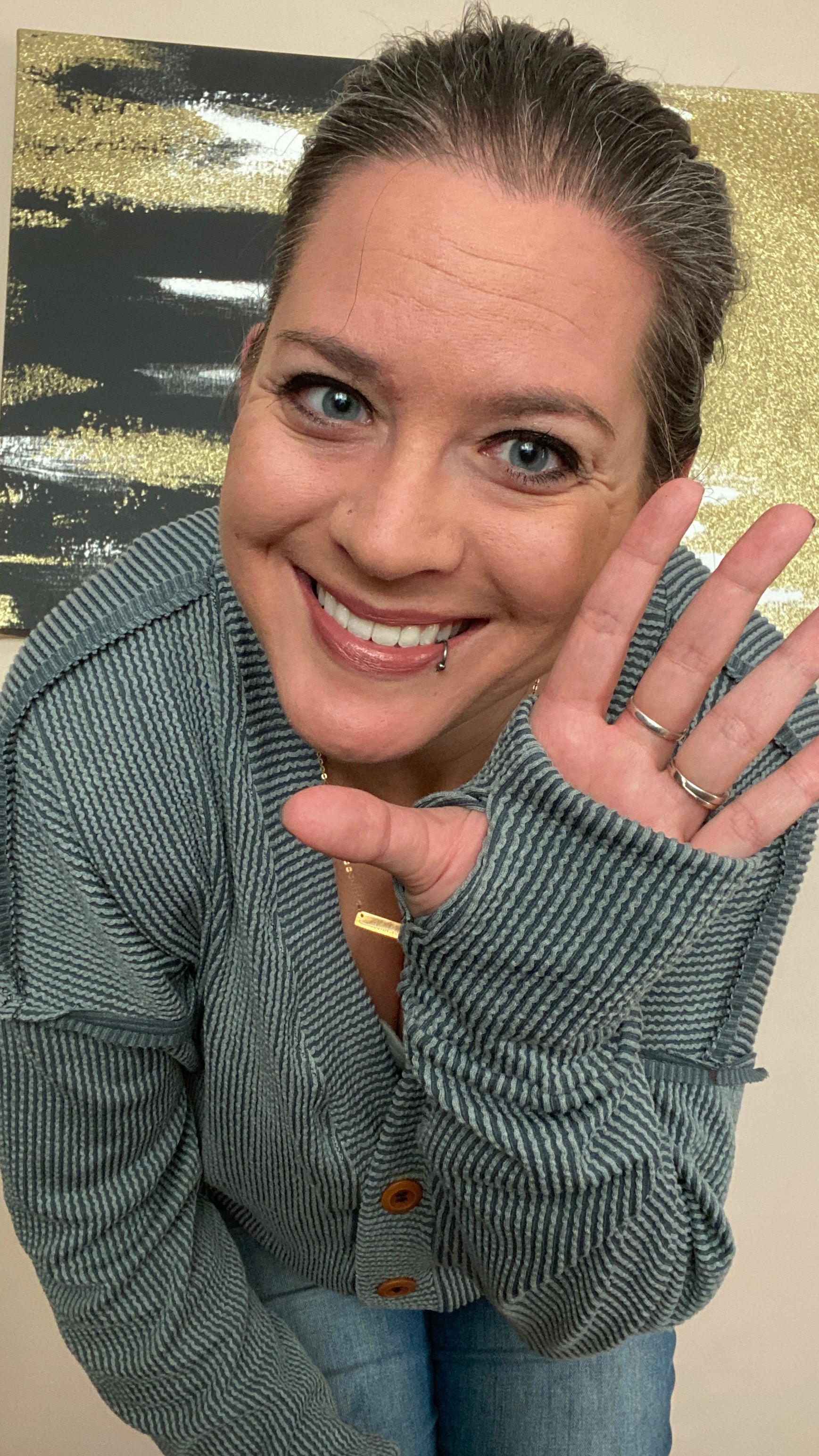 Woman wearing a green cardigan and blue jeans, waving with a thumbhole cuff detail.