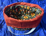 Fabric crock pot bag with a colorful interior lining on a blue background. This carrier was made using the warm and cozy slow cooker carrier pattern by Ellie and Mac sewing patterns.