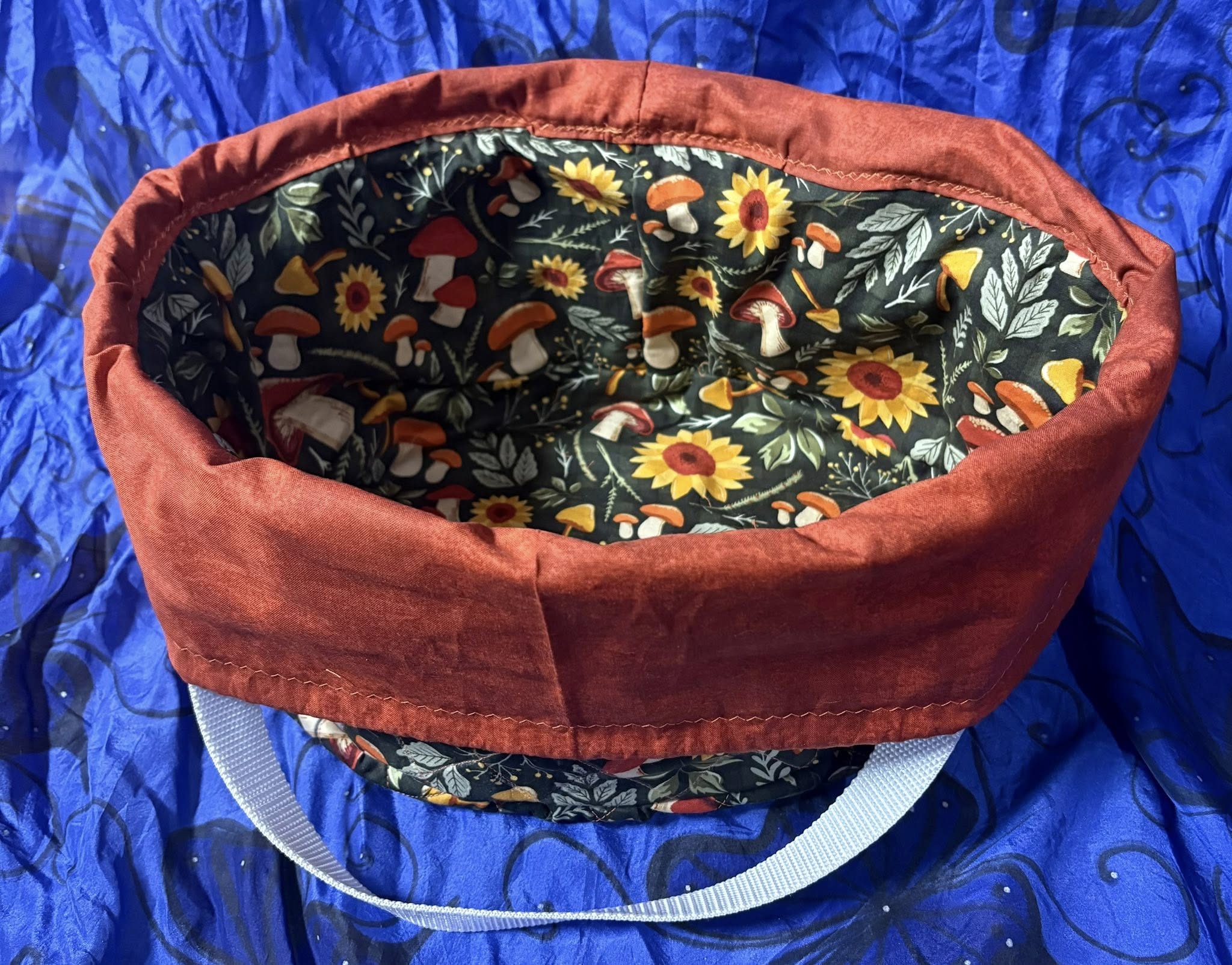 Fabric crock pot bag with a colorful interior lining on a blue background. This carrier was made using the warm and cozy slow cooker carrier pattern by Ellie and Mac sewing patterns.