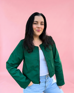 Woman wearing a green jacket made using the Harper Everyday Jacket Pattern and light blue jeans against a pink background