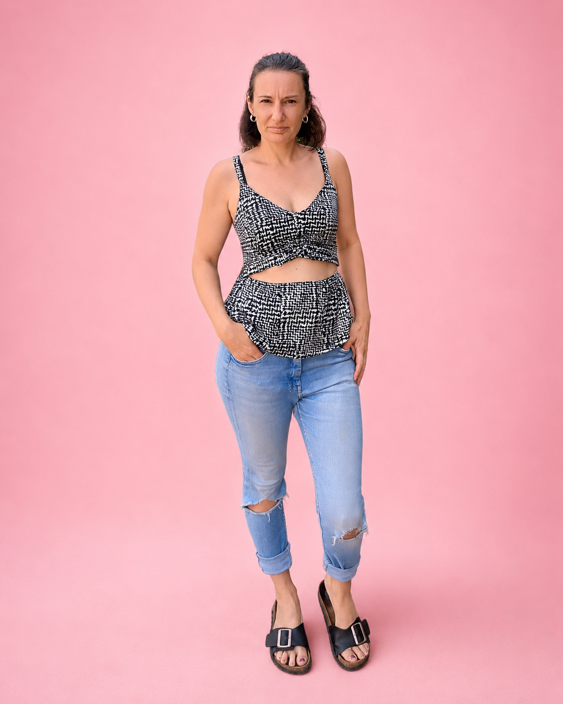 A woman modeling a matching black and white patterned ruched front peplum top with light-wash distressed jeans and black slide sandals, set against a solid pink studio background. Top was made using Ellie and Mac PDF sewing patterns. Easy sewing patterns for beginners. Includes A4, Letter, A0, and projector files. Sew along video included.