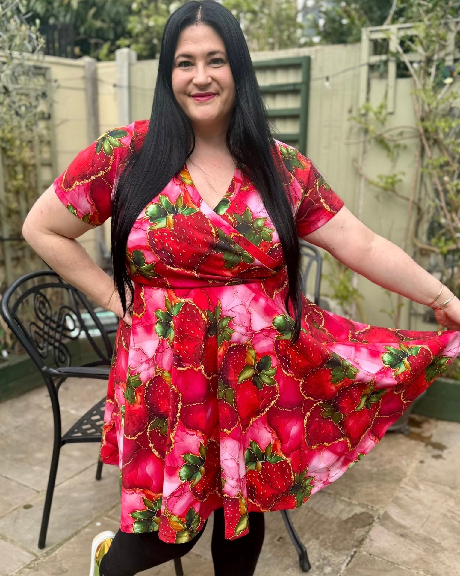 Woman wearing a red strawberry dress standing outdoors. Sewing pattern.