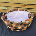 Colorful geometric-patterned fabric slow cooker carrier, open and empty, on a wooden surface. This carrier was made using the warm and cozy slow cooker carrier pattern by Ellie and Mac sewing patterns.