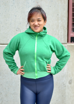 Woman in a city modeling a bright green athletic bomber jacket with zip closure and scuba hood. Cropped version. Ellie and Mac PDF sewing patterns.