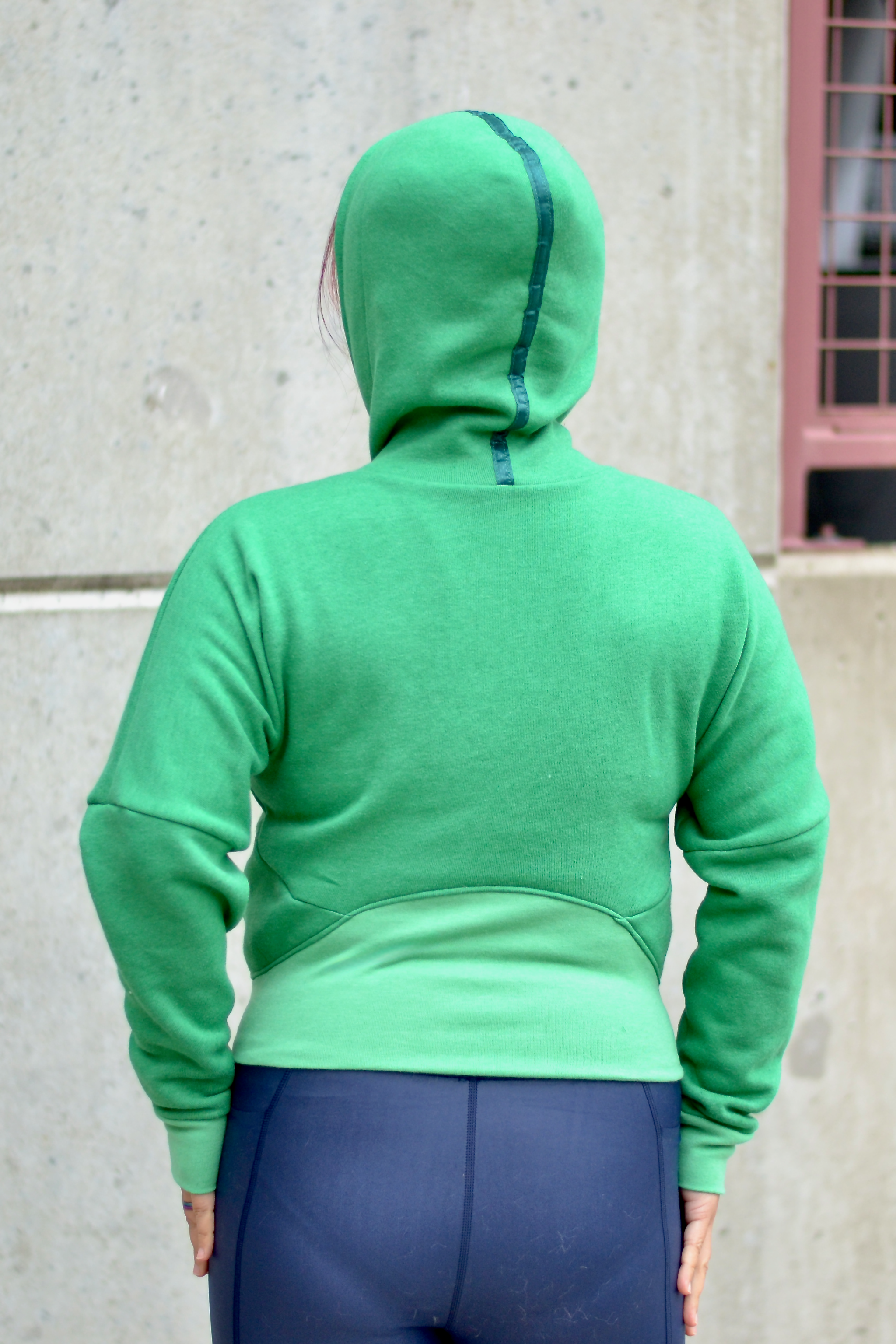 Woman in a city modeling a bright green athletic bomber jacket with zip closure and scuba hood. Cropped version. Ellie and Mac PDF sewing patterns.