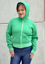 Woman in a city modeling a bright green athletic bomber jacket with zip closure and scuba hood. Cropped version. Ellie and Mac PDF sewing patterns.