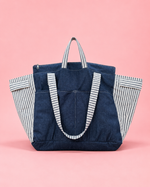 Navy tote bag with striped handles and sides on a pink background. Great upcycle sewing project. 