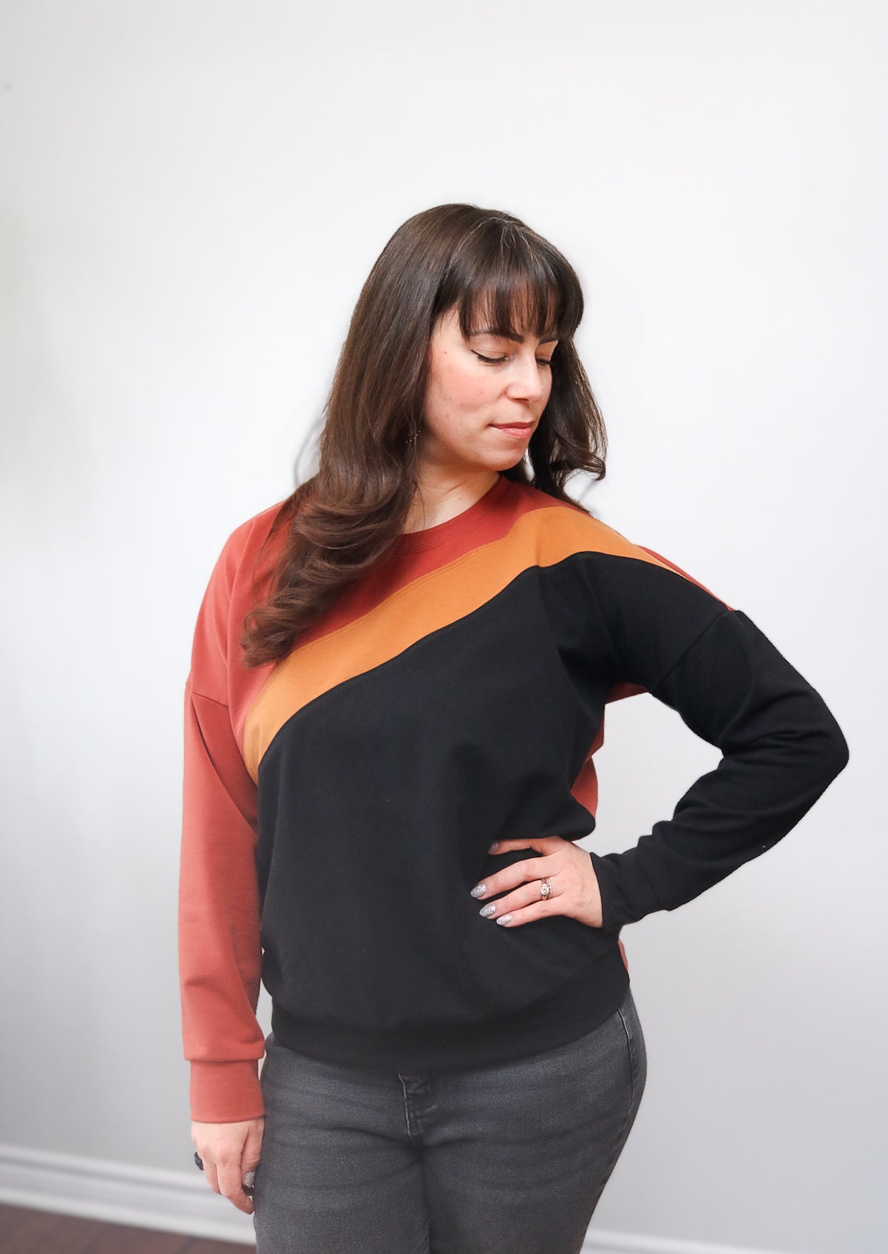 Woman wearing a color-blocked sweater with orange, black, and rust design against a white background. Made using the Ellie and Mac Sewing Pattern - Sage Diagonal Color-Block Sweatshirt pattern.