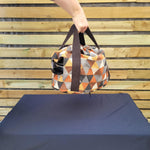 Person holding a geometric-patterned slow cooker carrier bag against a wooden fence background.