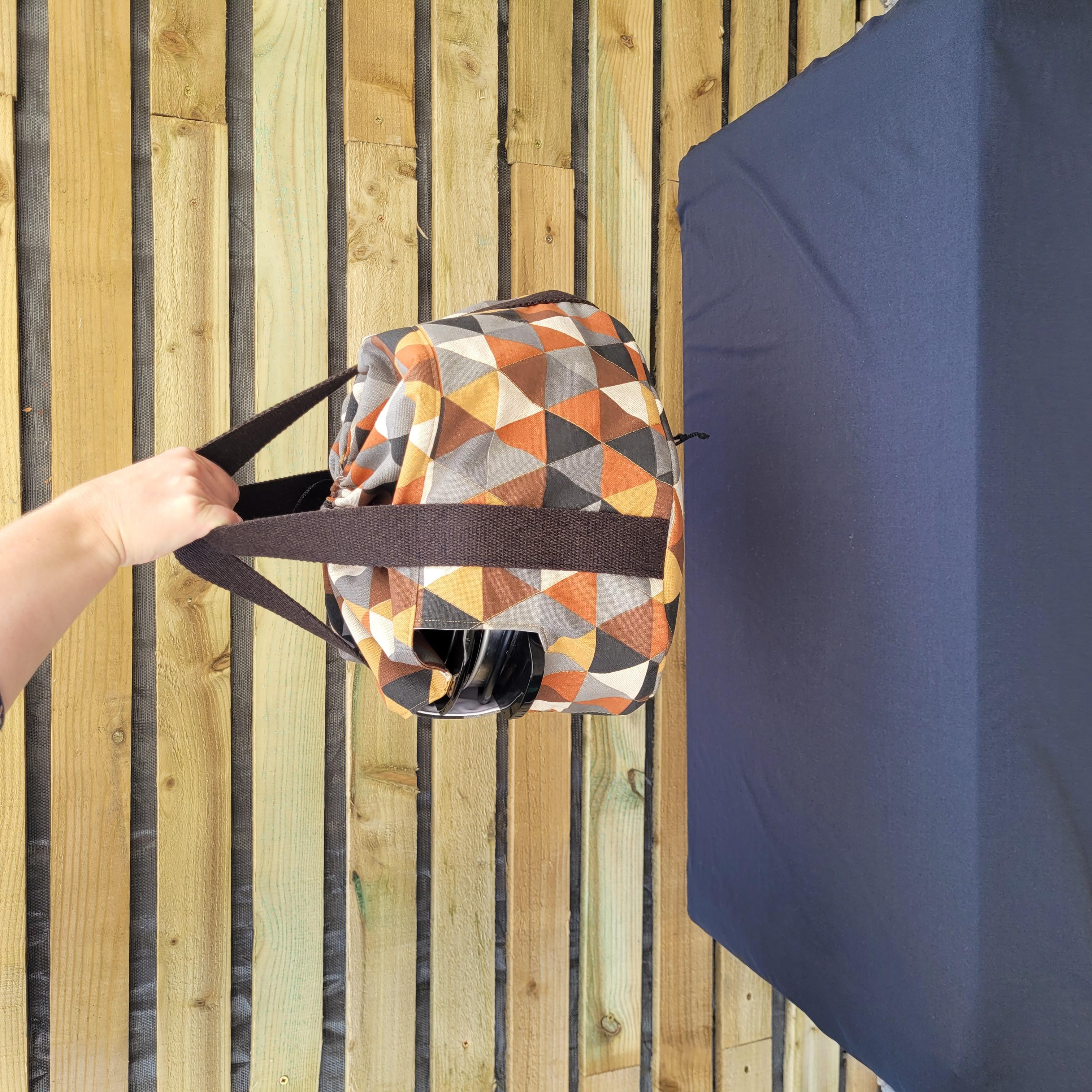 Person holding a geometric-patterned slow cooker carrier bag against a wooden fence background.
