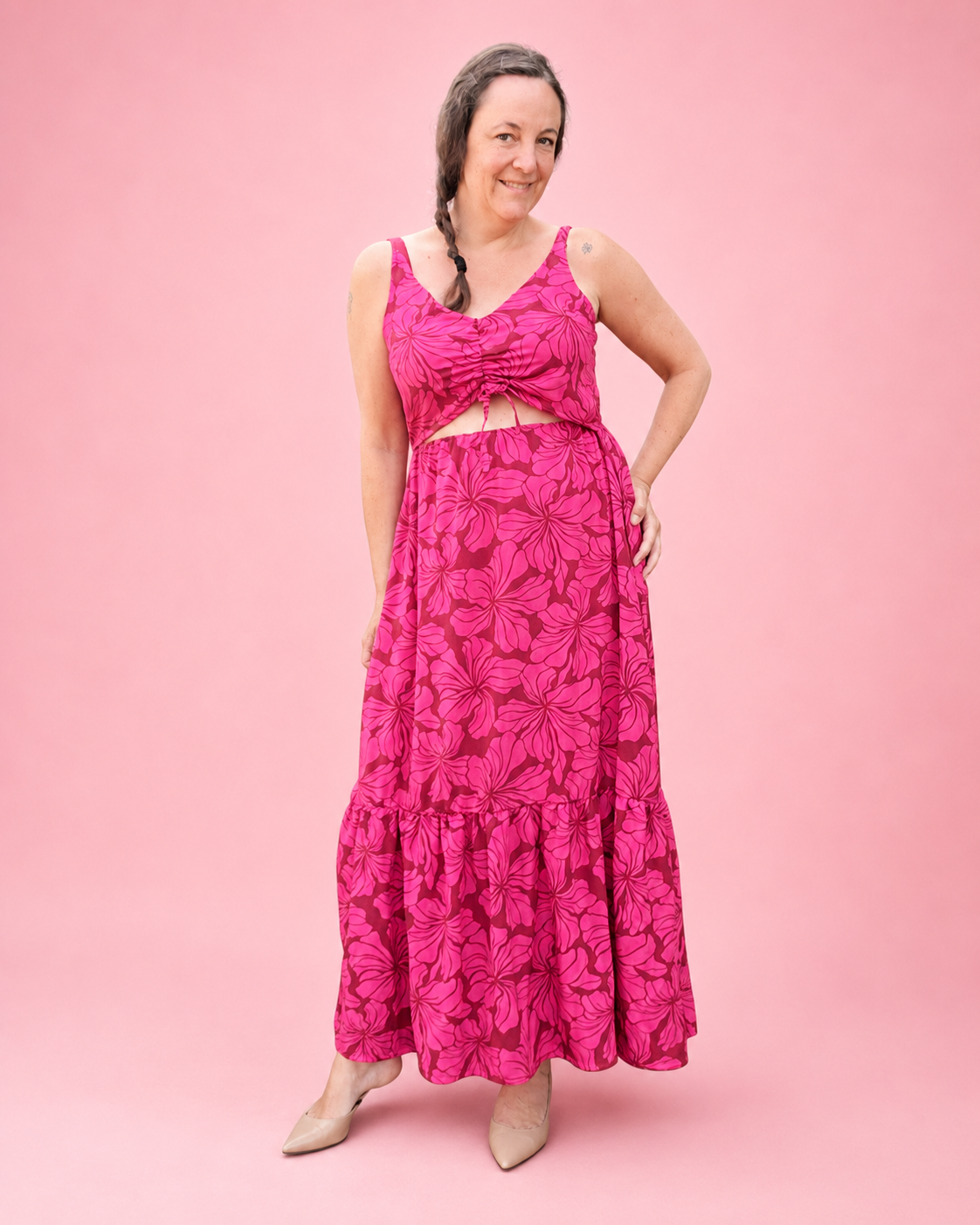 A woman modeling a bright pink maxi woven sundress with a front cutout and a matching tiered maxi skirt, both featuring a dark pink floral pattern, set against a solid pink background. Ellie and Mac sewing patterns are easy and flattering with an inclusive size chart. 