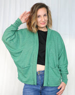 Woman wearing a green checkered oversized cardigan over a black top and blue jeans on a white background. Cardigan is made using Ellie and Mac's Celeste Batwing Cardigan PDF sewing pattern