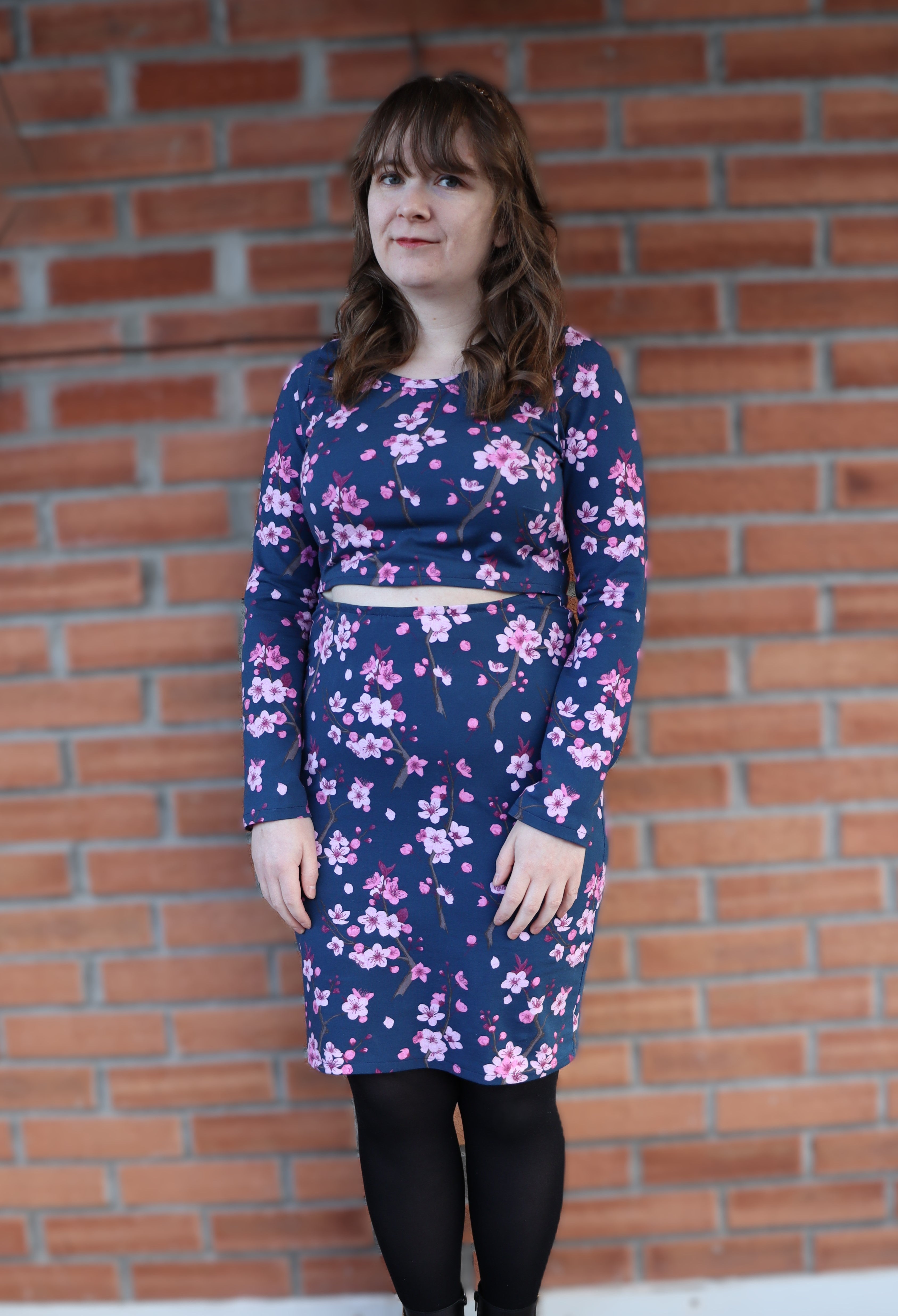 Woman wearing a blue floral dress standing against a brick wall. PDF pattern