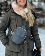 Person wearing a green coat and carrying a blue phone bag in a snowy setting