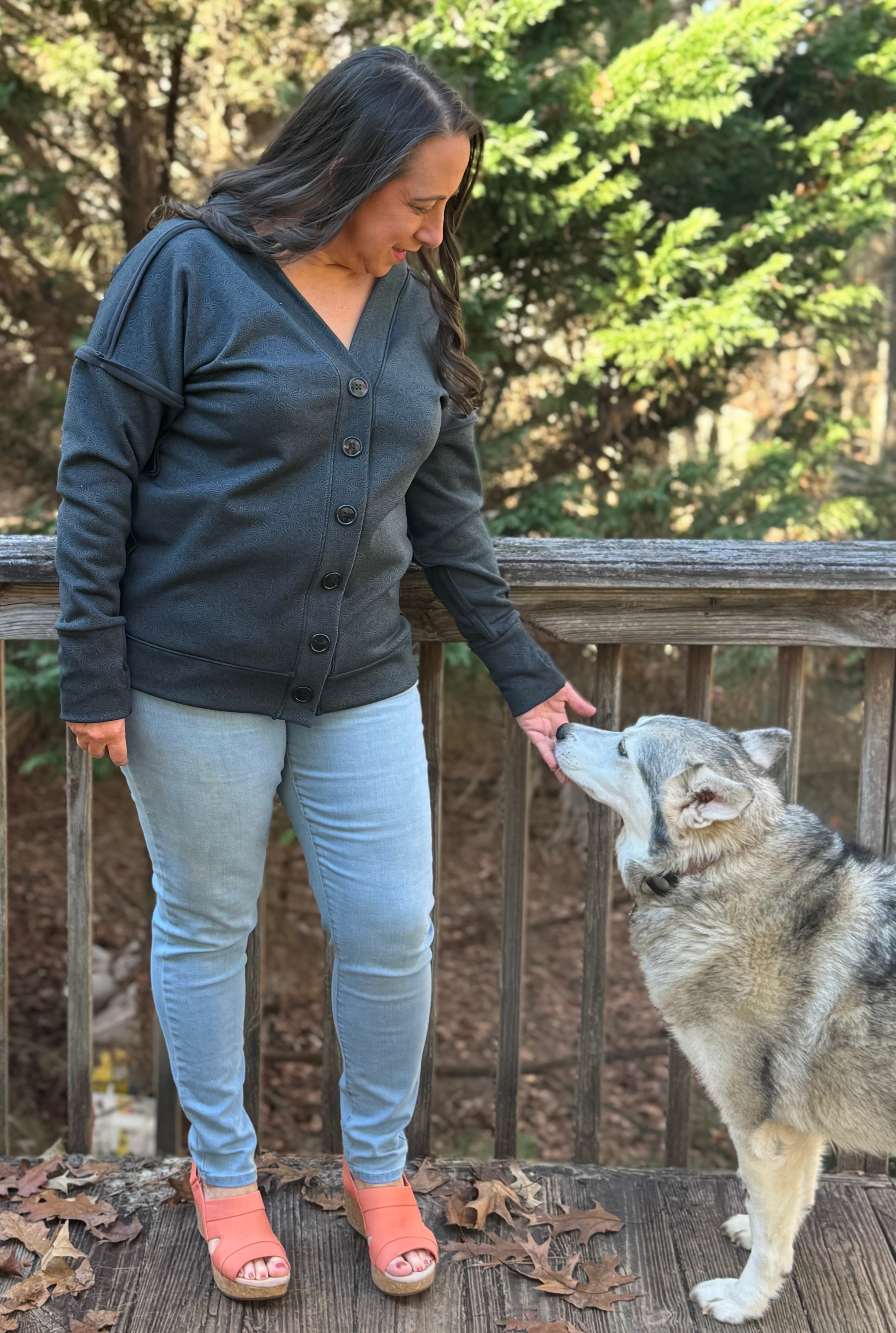 Woman in a gray Brielle Boxy Cardigan and light blue jeans standing on a wooden deck with a dog.