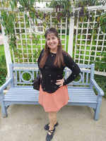 Woman standing next to a blue bench in a garden setting wearing an orange bubble skirt and black top for Halloween.