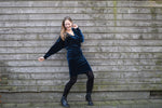 Woman in a blue velvet crossover wrap dress posing against a wooden wall with a big smile on her face.