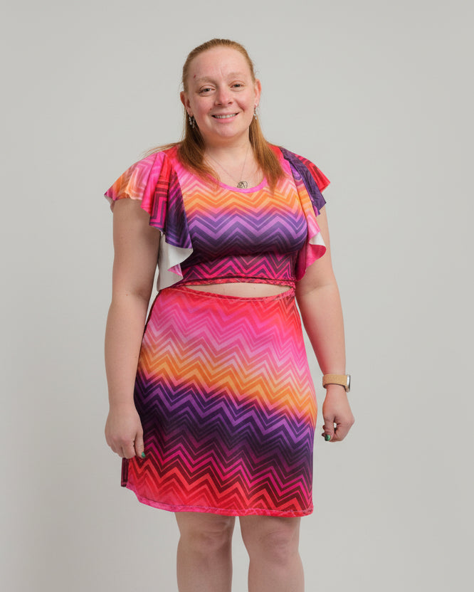 Person wearing a colorful dress standing in front of a brick wall.