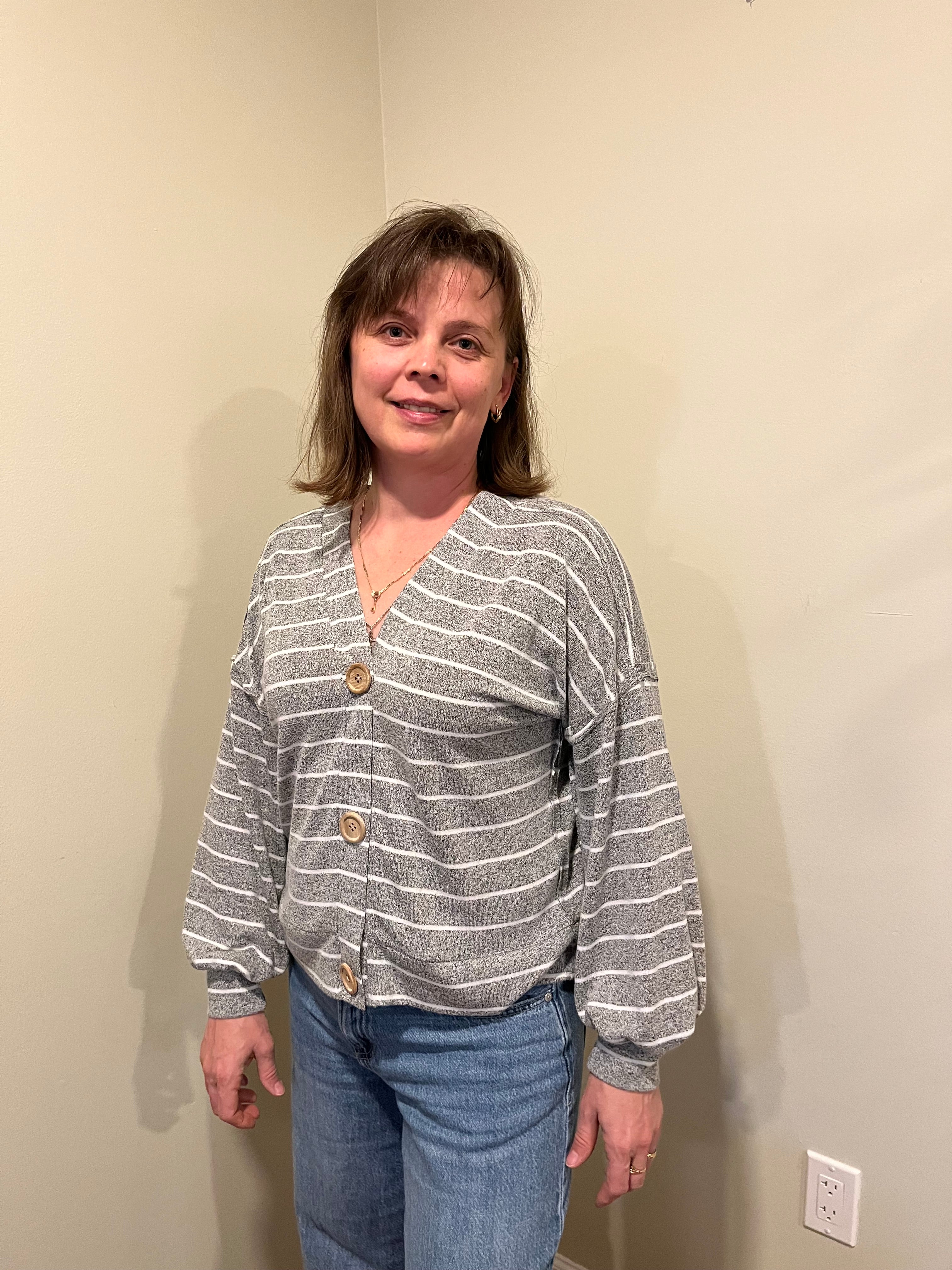 Person wearing a striped shirt and jeans standing against a plain wall.
