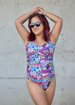 Woman wearing a colorful swimsuit with a graphic design against a concrete wall.