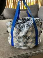 Patterned slow cooker carrier bag with blue straps on a textured surface.