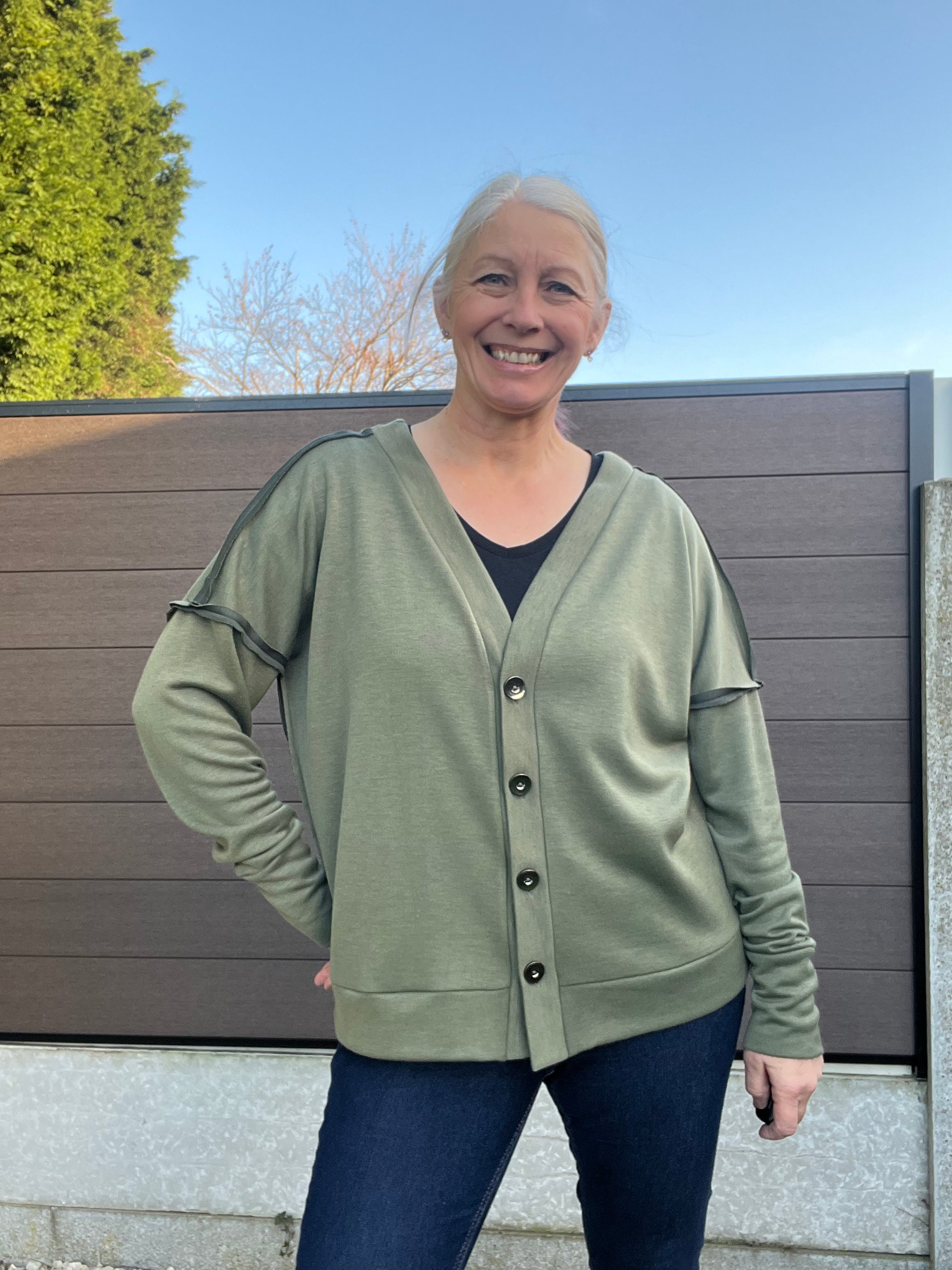 Person wearing a green oversized cardigan in high hip length standing outdoors with a clear blue sky.