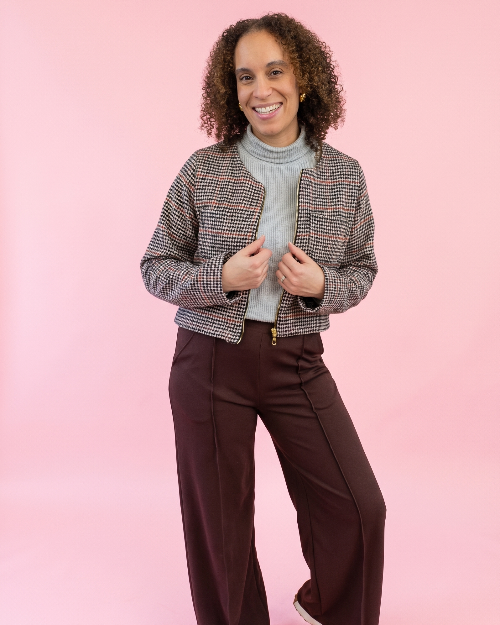 Woman wearing a checkered jacket and brown pants on a pink background