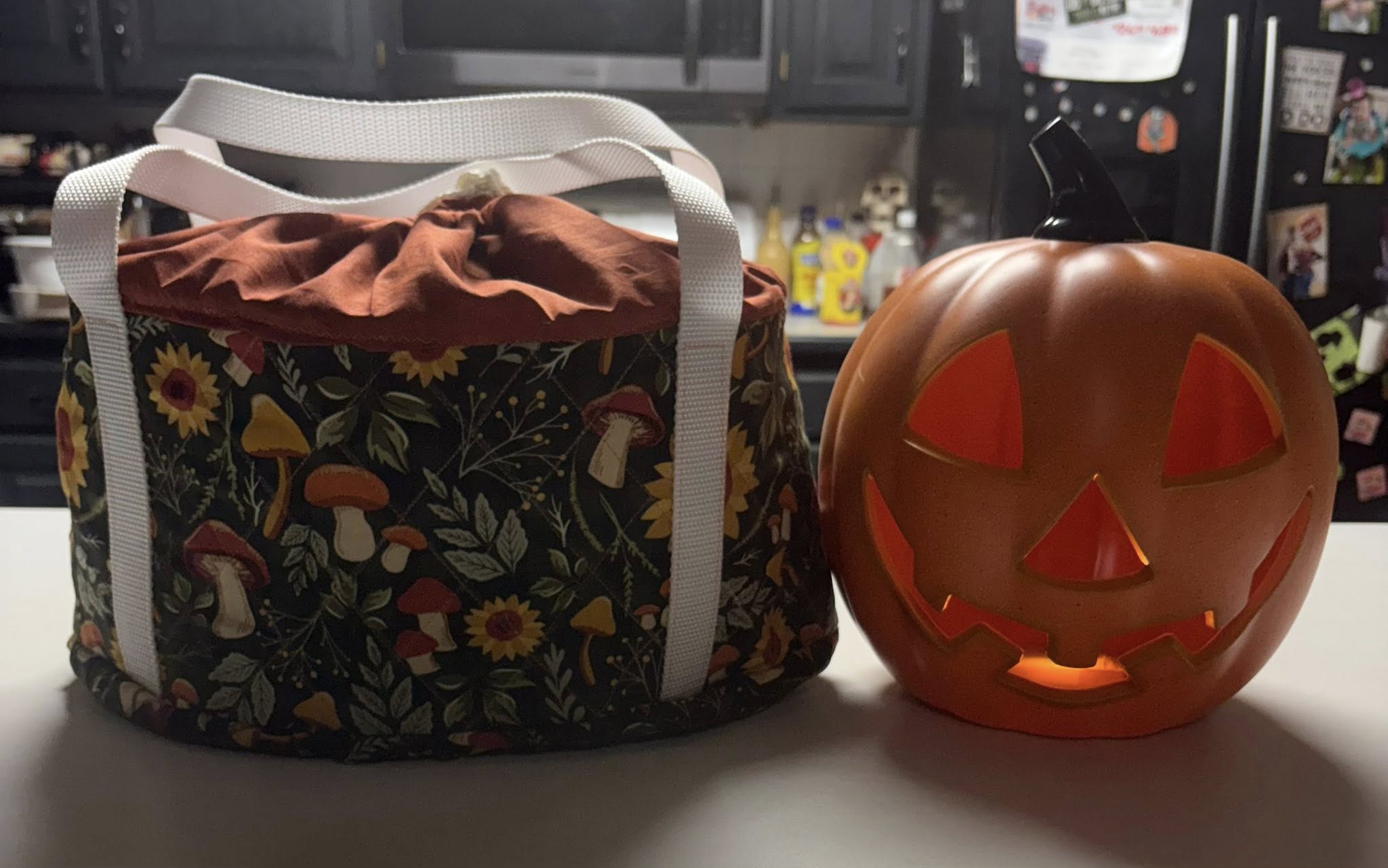 Fabric slow cooker bag with floral pattern next to a ceramic jack-o'-lantern on a kitchen counter.