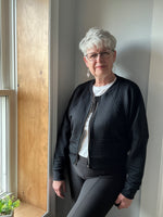 Woman inside by window modeling a black textured fabric knit bomber jacket with zip closure. Athletic Cropped version. Ellie and Mac PDF sewing patterns.