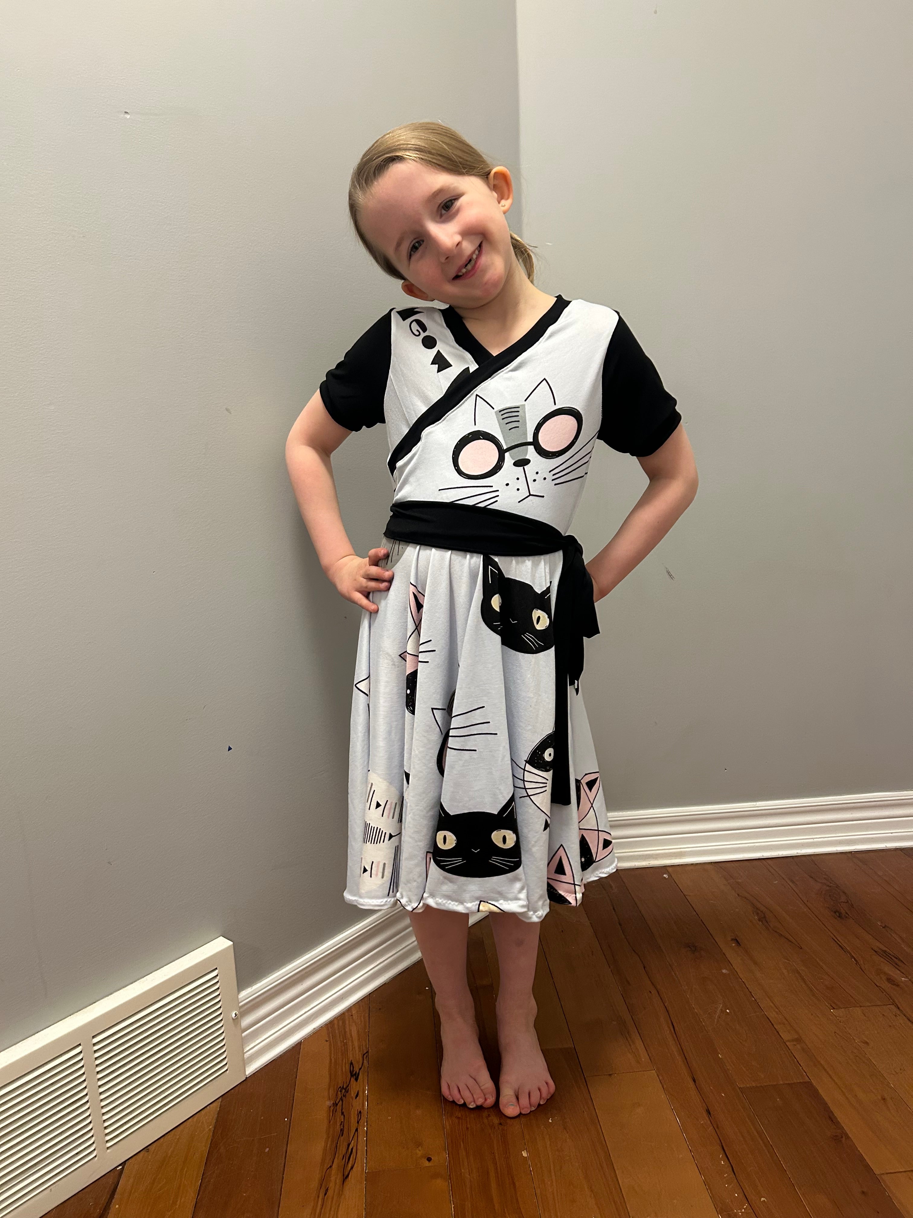 Cat print fabric in the Tres Belle Dress sewing pattern by Ellie and Mac Patterns. Easy for beginners. A0 A4 Letter and Projector files with sew along video tutorial.

Short banded sleeves with faux wrap bodice, circle skirt, and sash.

