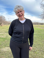 Woman modeling a black athletic raglan bomber jacket with zip closure. Regular cuffs, curved band, and cropped version. Ellie and Mac PDF sewing patterns.