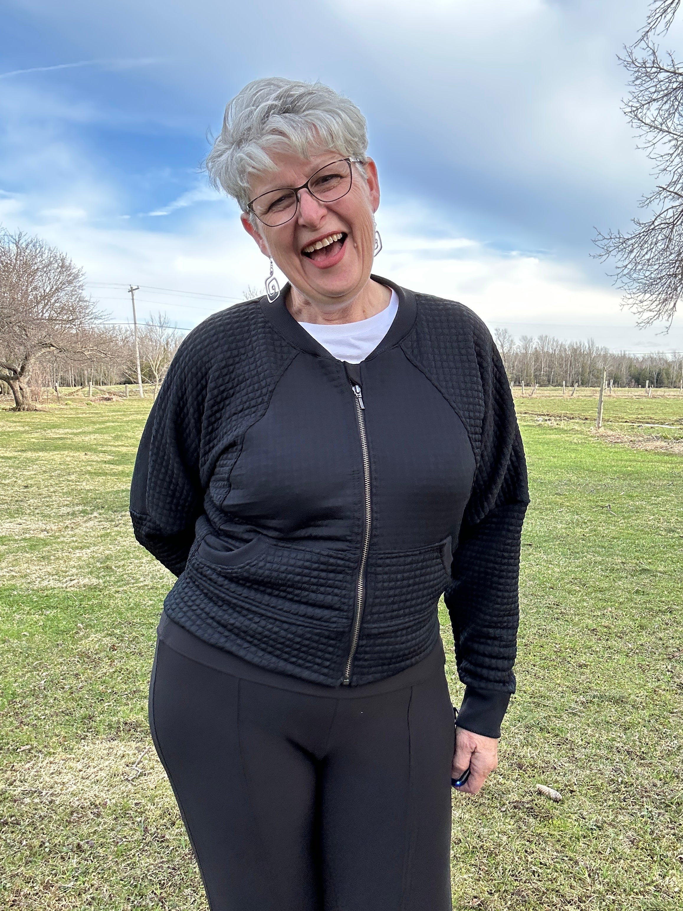 Woman modeling a black athletic raglan bomber jacket with zip closure. Regular cuffs, curved band, and cropped version. Ellie and Mac PDF sewing patterns.