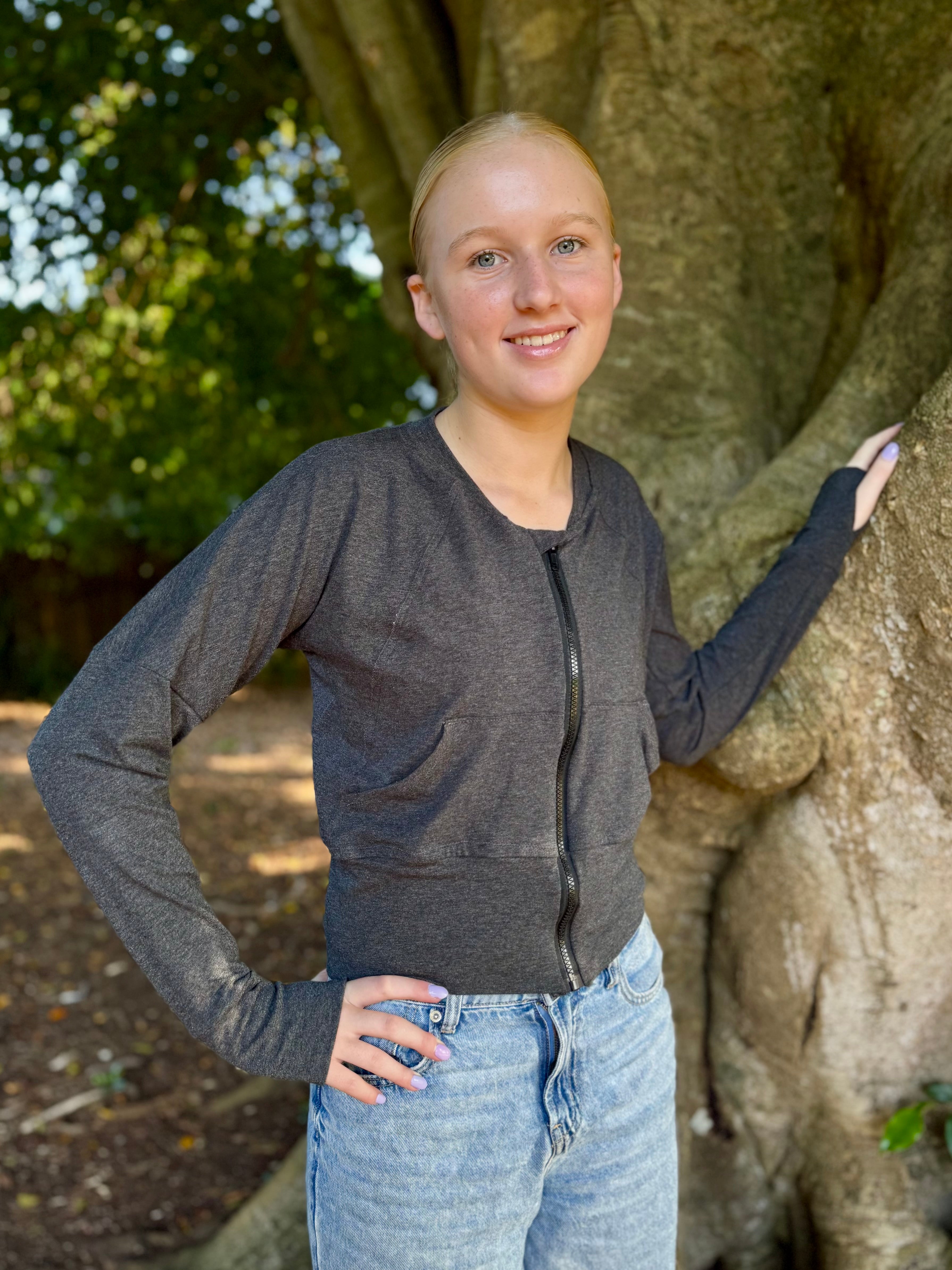 Teen girl outside modeling a solid grey raglan bomber jacket with zip closure, kangaroo pocket detail, and cuffs. diy jacket. 